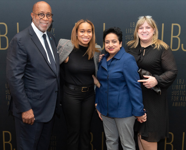 Eine Gruppe von vier Personen, die auf einem roten Teppich stehen, lächeln und für ein Foto posieren, mit einem "Liberty Justice for All Awards"-Schild im Hintergrund.