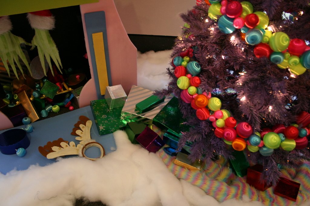 Drinnen ein geschmückter Weihnachtsbaum rechts, Geschenkboxen und Deko in der Mitte, eine Hütte mit Deko oben links und Baumwolle und Wolle unten.