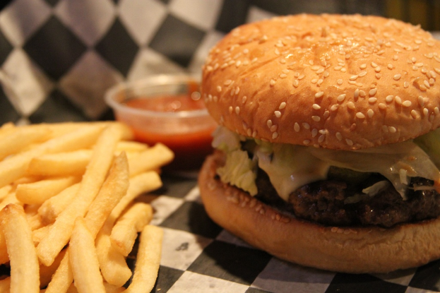 Ein Burger, eine Portion Pommes und ein kleiner Behälter mit Sauce auf einem Tisch.