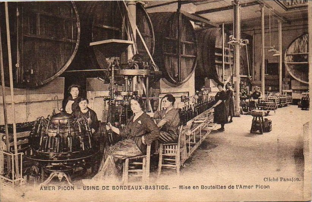 Schwarzes und weißes Foto von Frauen bei der Arbeit in einer Fabrik, mit Maschinen und sitzenden Personen, mit dem Text "Amer Picon - Use de Bordeaux-Bastide" unten.