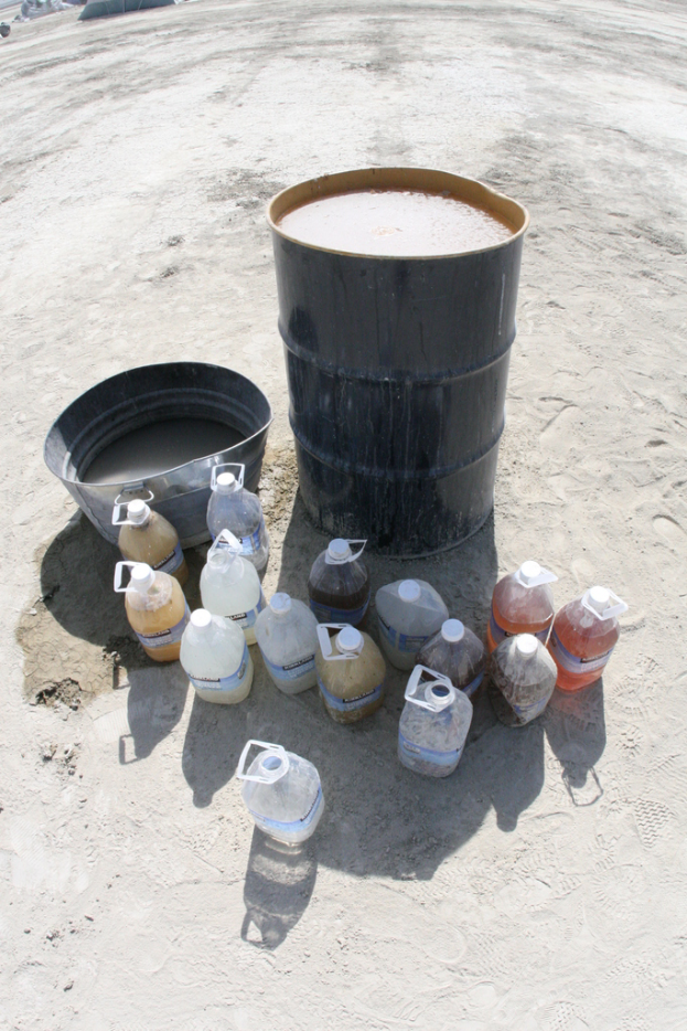 Eine Trommel und ein Eimer stehen nebeneinander, umgeben von mehreren flüssigkeitsgefüllten Dosen auf dem Boden.