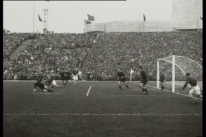 Ein Schwarz-Weiß-Foto eines Fußballspiels im Stadion, mit Spielern auf dem Feld und einem Torpfosten auf der rechten Seite, Zuschauern in den Rängen, Fahnen und einem klaren Himmel, mit Text oben und unten: "1958-1958 WM-Finale - Manchester United v Liverpool."
