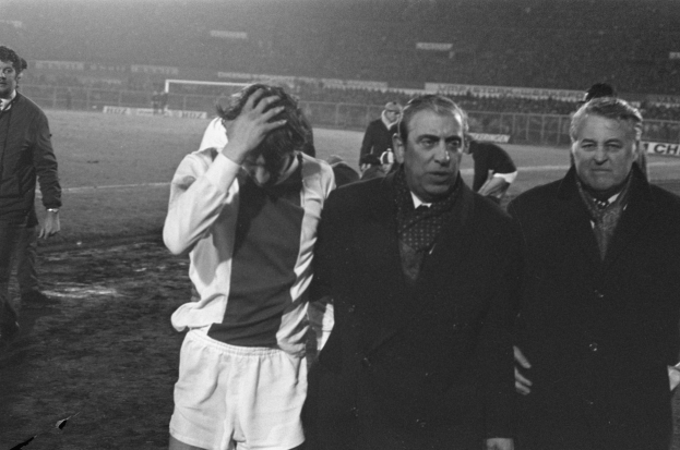 Eine Gruppe von Männern in Schwarz-Weiß-Kleidung steht zusammen auf einem Fußballfeld, im Hintergrund ist ein Stadion zu sehen, wahrscheinlich nach einem gewonnenen Spiel.