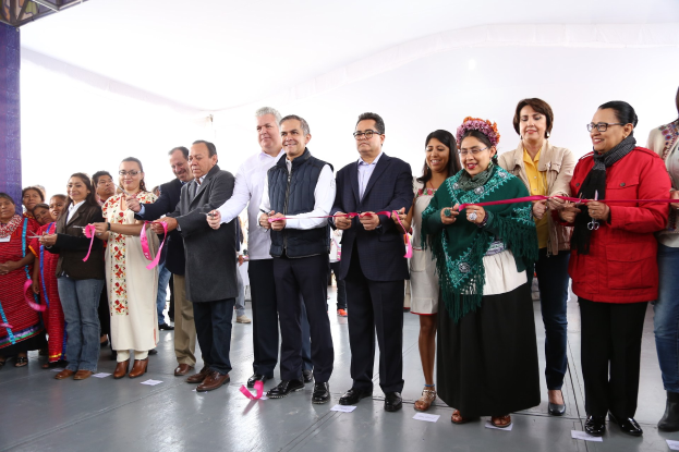 Eine Gruppe von Menschen bei einer Scherenschnitte-Zeremonie, mit Scheren in der Hand, Papieren auf dem Boden und einem weißen Tuch im Hintergrund.
