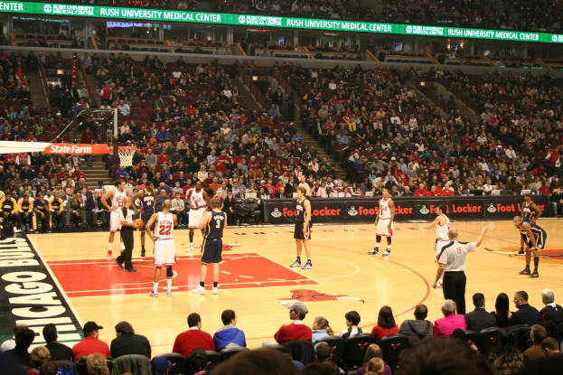 Eine Gruppe von Menschen in einem Stadion, einige halten einen Basketball, andere schauen von den Rängen und Werbung ist auf den Werbetafeln zu sehen.