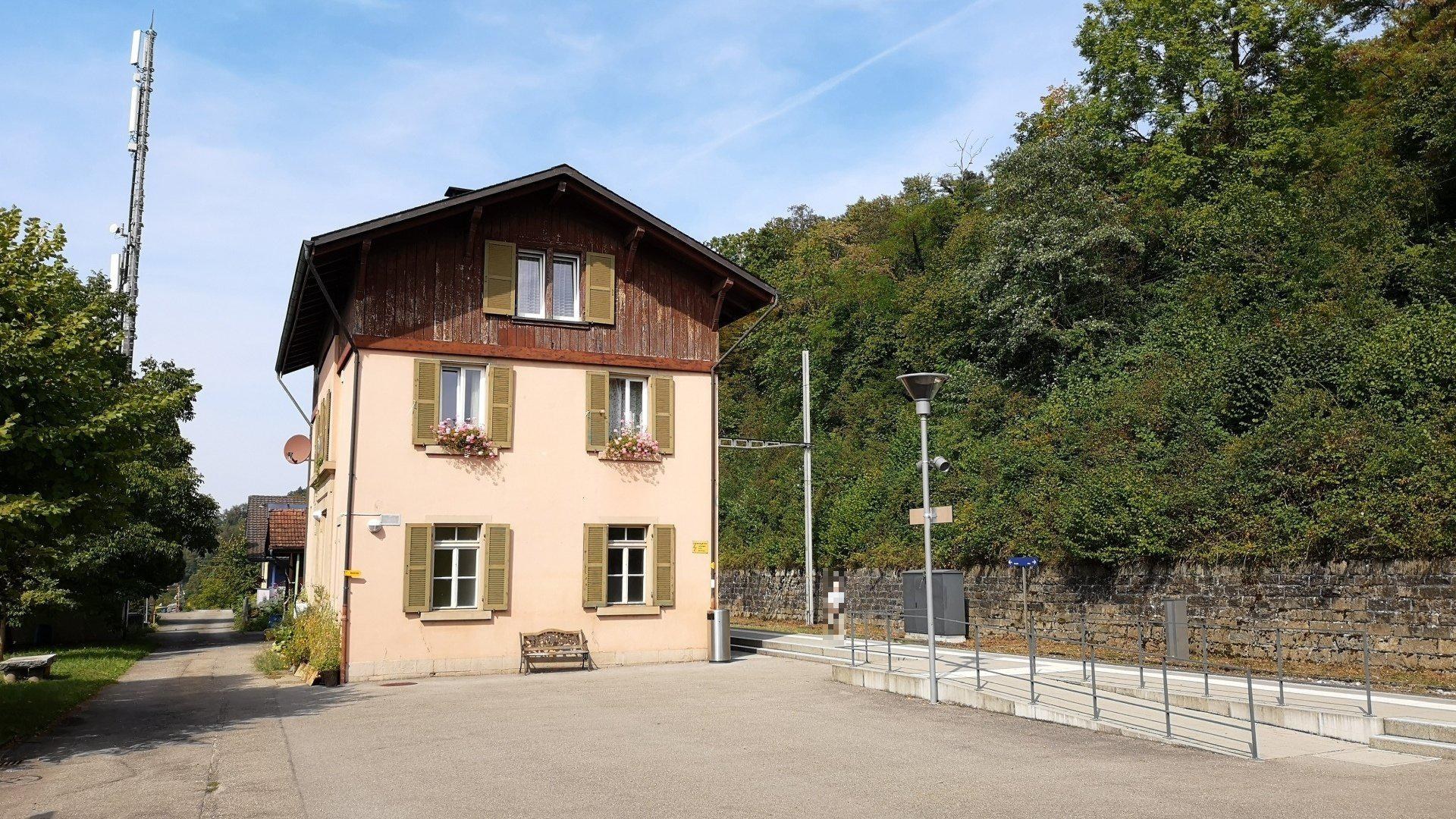 Ferienhaus in Baden-Württemberg, Deutschland zum Verkauf, mit einem mehrfenstrigen Gebäude mit einer vorderen Einfriedung, umgeben von Straßenmöbeln, Grünflächen und einem bewölkten Himmel.