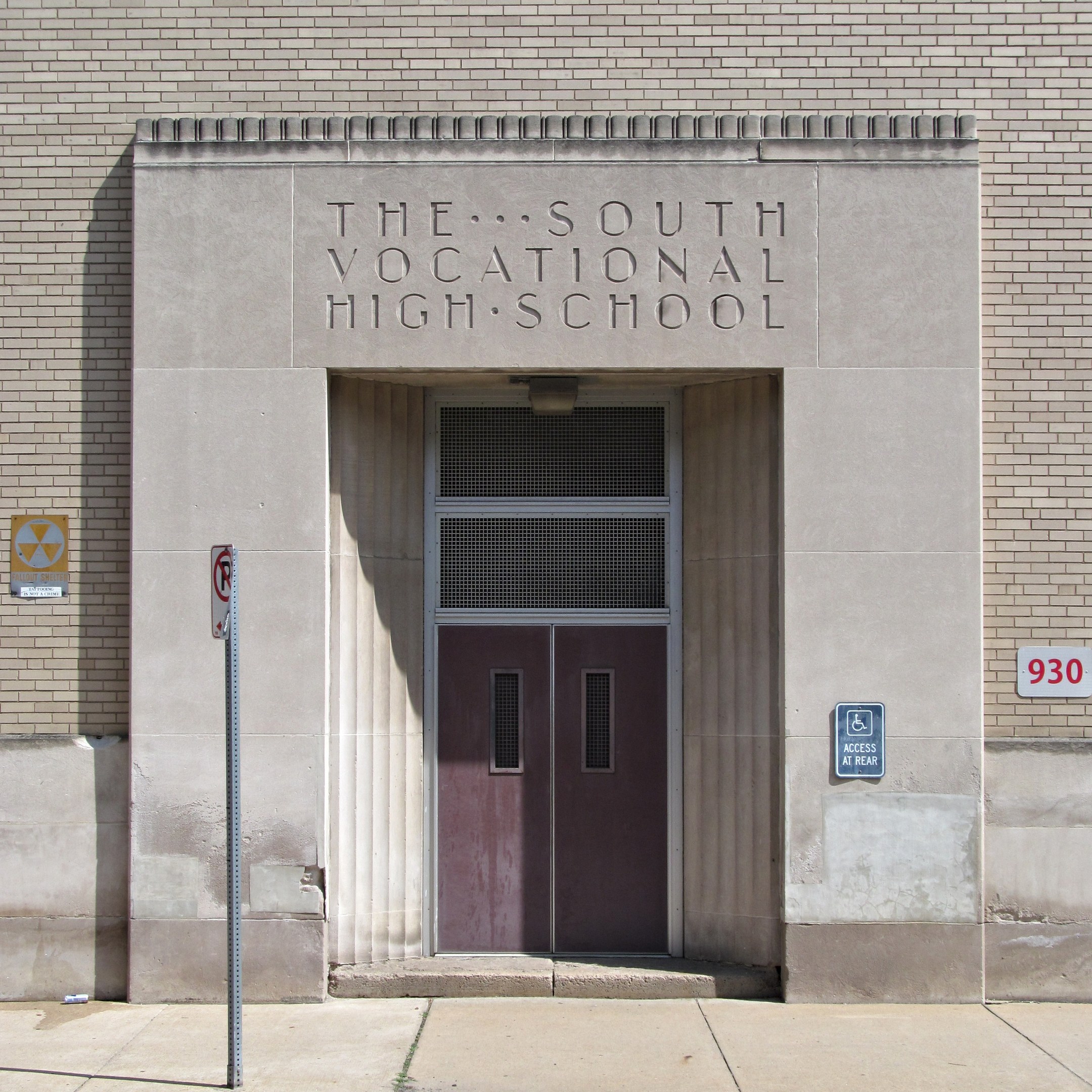Das Südliche Berufsbildungszentrum mit einer Tür, Schildern an der Wand und einem Weg, der zur Eingangstür führt.