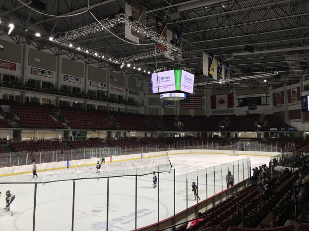 Hockey-Spiel in einer großen Arena mit einem zentralen Netz, Zuschauern auf beiden Seiten, Deckenbeleuchtung, Trägern und Bannern an den Wänden, identifiziert als die St. Louis Blues Arena.