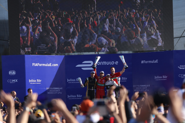 Podium mit Menschen mit Pokalen bei der FIA-Formel-E-Veranstaltung in Mexico City, mit Werbetafeln und einem Bildschirm im Hintergrund.