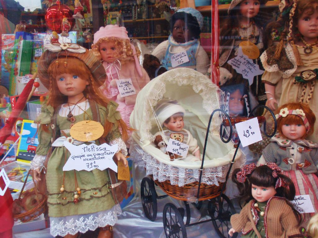 Eine Ausstellung mit mehreren Barbie-Puppen in verschiedenen farbenfrohen Kleidern neben einem Rollstuhl, Kisten, einem Schirm, Ständern, Bannern und anderen Produkten.