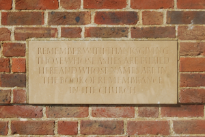 Eine Backsteinmauer mit einer Gedenktafel, auf der steht: "Erinnere dich mit Dankbarkeit an diejenigen, deren Asche hier begraben ist und deren Namen im Buch der Erinnerung in der Kirche stehen."
