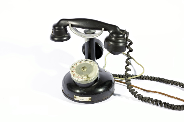 Ein schwarzes Telefon mit Zahlen und Text, der durch die Glasfläche sichtbar ist, verbunden durch Kabel, vor einem weißen Hintergrund.