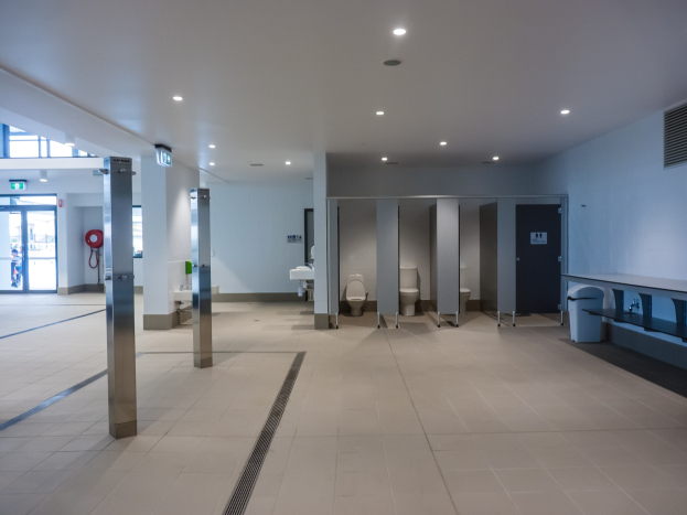 Große ßeße Toilette mit mehreren Toiletten, tragenden Säulen, einem Mülleimer, einer Tür, einem Schild, einem Feuerlöscher und Deckenleuchten unter einem Dach.