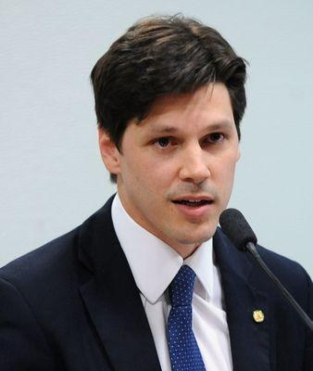 Ein Mann im Anzug und Krawatte spricht in ein Mikrofon und scheint eine Regierungsentscheidung zu kommentieren.