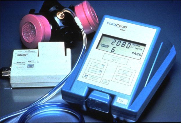 Eine Gasmaske auf einem Tisch neben einem elektronischen Gasdetektorgerät, das über ein Kabel verbunden ist.