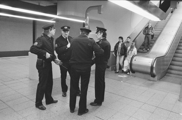 Gruppe von Polizisten in einer U-Bahn-Station mit einer Rolltreppe auf der rechten Seite und Deckenbeleuchtung.