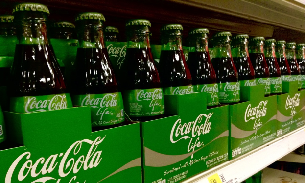 Glasflaschen werden in grüne Kartons mit 'Coca-Cola Life' daraufgestellt.