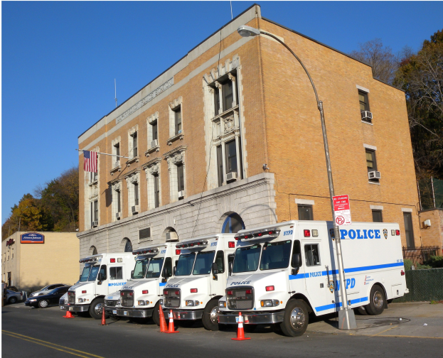 Polizeifahrzeuge vor einem Gebäude mit einer Tafel, Verkehrskegeln, einer Flagge, Bäumen und einem Zaun geparkt.