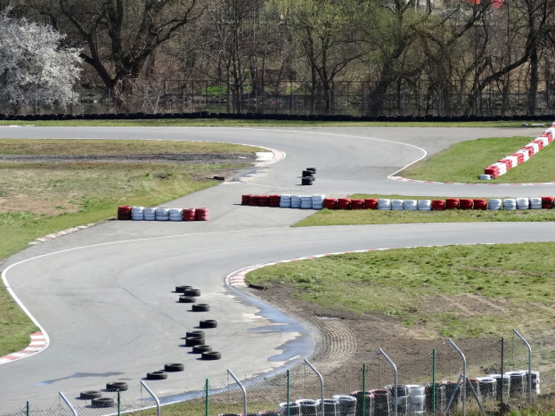Rennstrecke voller gestapelter Reifen, umgeben von Gras und Maschendrahtzaun, mit Bäumen im scenischen Hintergrund.