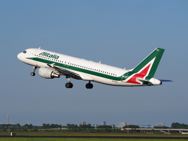 Ein Airbus A320-232 der Alitalia mit dem Kennzeichen ERJ-EJZ beim Starten am Frankfurter Flughafen, grüne Wiesen darunter, Bäume und Gebäude im Hintergrund und einen klaren blauen Himmel.