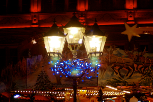 Eine Straßenlaterne in einer nächtlichen Stadt, dekoriert mit Lichtern und Schmuck, steht vor einem Gebäude und verbreitet eine festliche Atmosphäre.