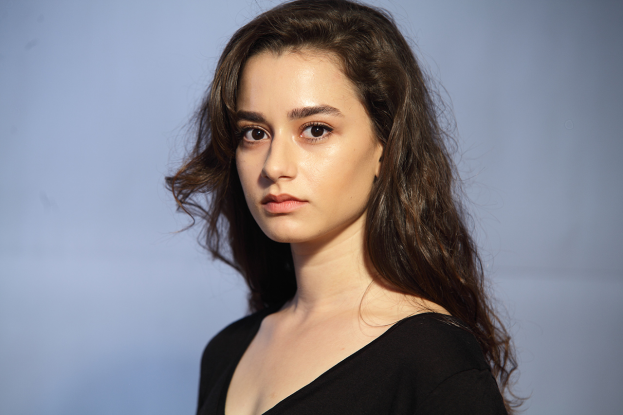 Eine Frau in einem schwarzen Kleid mit einem eleganten Bob-Haarschnitt, dezentem natürlichem Make-up und einer selbstbewussten Haltung posiert vor einem weißen Hintergrund.