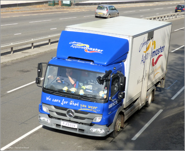 Eine Straße mit wenigen Fahrzeugen, einer mittigen Begrenzung und einer Metallkonstruktion oben.