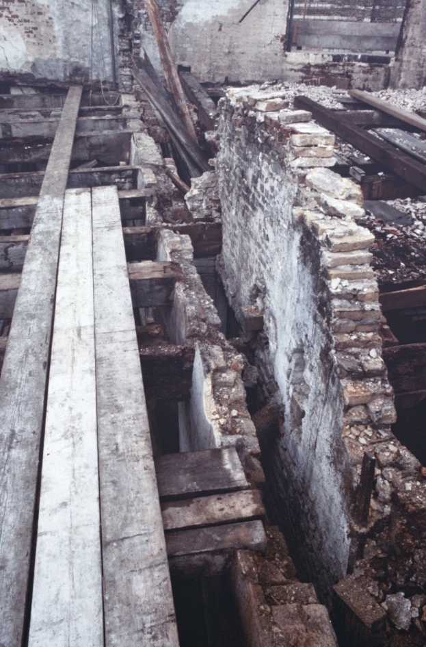 Alter Bau wird abgerissen mit verstreuten Holzplanken und Steinen im Vordergrund und einer verbliebenen Wand im Hintergrund.