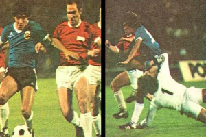 Eine Gruppe von Männern, die auf einem Feld Fußball spielen, wobei einer den Ball tritt und andere versuchen, die Kontrolle zu erlangen, vor einer Tafel in einem Stadion.