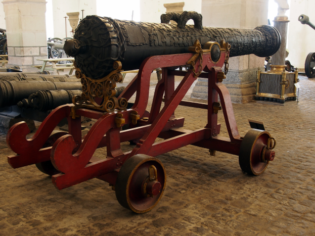 Ein altes Geschütz in einem Museum ausgestellt, umgeben von anderen Geschützen und Pfeilern im Hintergrund.