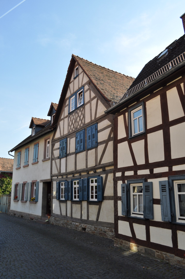 Eine Kopfsteinpflasterstraße mit Fachwerkhäusern in Colmar, Elsass, Frankreich, unter einem klaren blauen Himmel.
