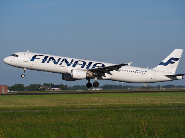 Ein Airbus A320-200 der Finnair, der vom Frankfurter Flughafen abhebt, mit Gras darunter, Gebäuden und Bäumen im Hintergrund und einem klaren blauen Himmel darüber.