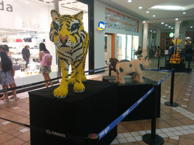 Statuen von Tieren auf schwarzen Kisten, umgeben von Pfählen mit Gummibändern, mit Geschäften, die Taschen, Schuhe und andere Gegenstände anbieten, und Menschen, die herumlaufen.
