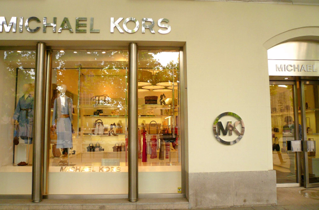 Ein Michael Kors Store in New York City mit Glaswänden und -türen, auf denen Schaufensterpuppen in Kleidern und Regale mit Handtaschen zu sehen sind, mit einem Schild, das eine bevorstehende Eröffnung ankündigt.